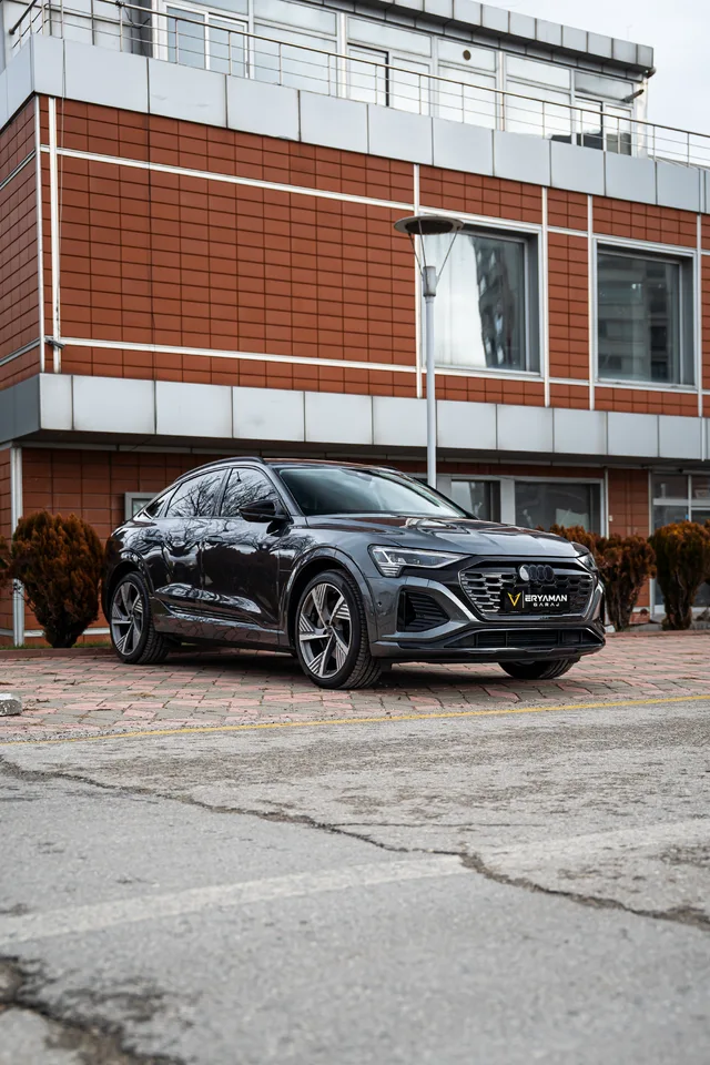 Kırmızı cepheli bir binanın önünde koyu renk Audi